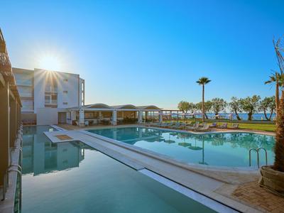 Luxury hotel pool with lounge chairs, palm garden, and clear sky at sunset.