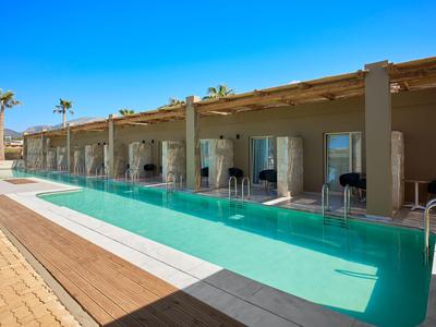 Modern outdoor pool with lounge chairs in front of hotel rooms under clear sky.
