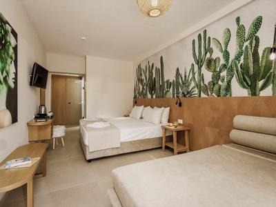 Modern hotel room with cactus wall art, double bed, sofa, and desk.