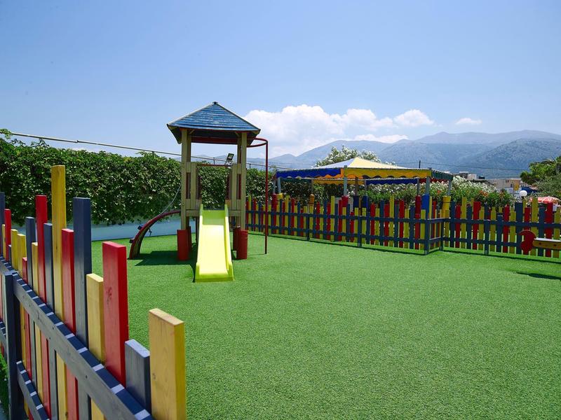 Kinderspielplatz mit bunter Umzäunung, Rutsche und Kletterturm auf grünem Kunstrasen.