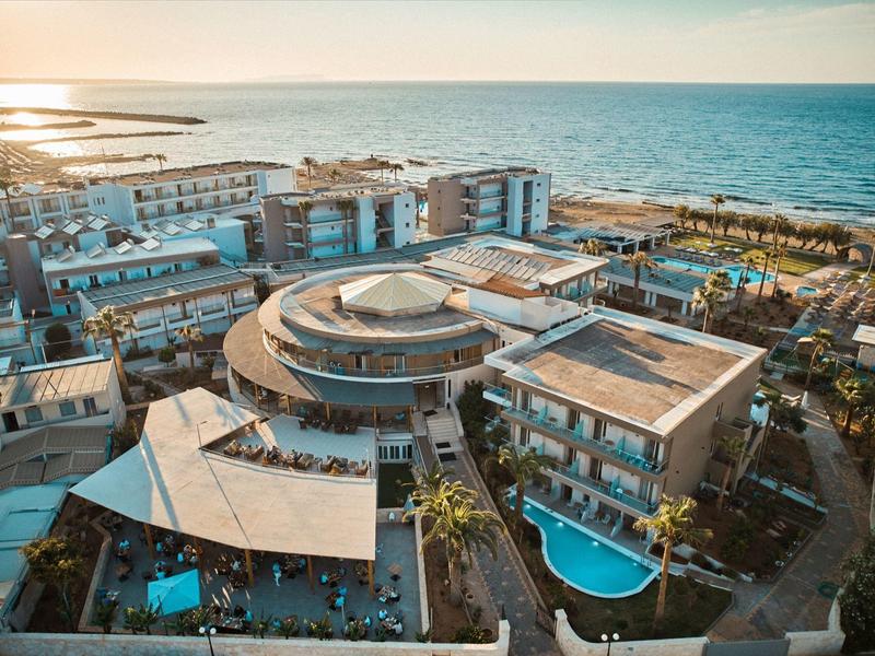 Moderne Hotelanlage mit rundem Gebäude, Pool und Blick aufs Meer bei Sonnenuntergang.