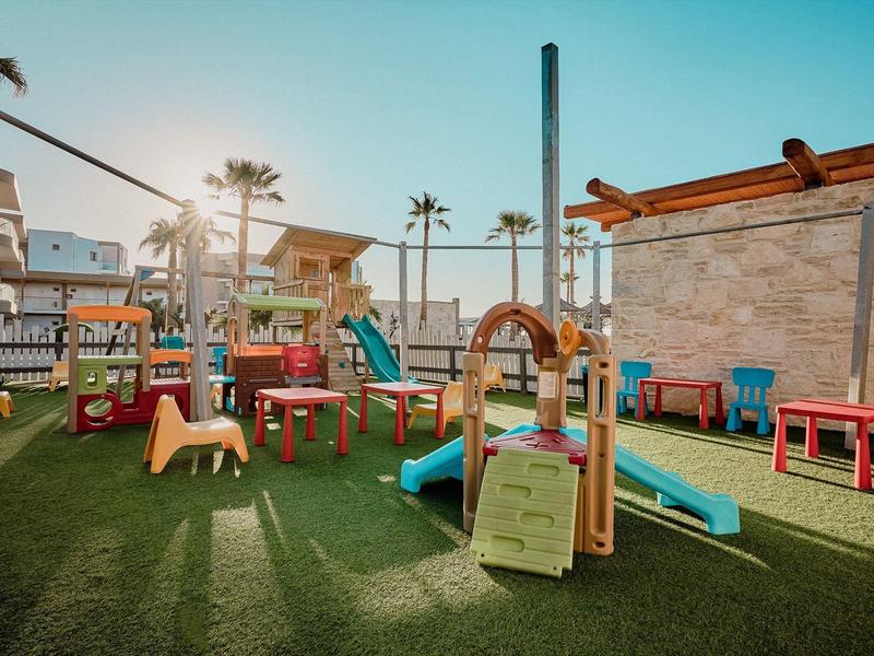 Kinderspielplatz mit Rutschen, Klettergerüst und bunten Sitzmöbeln auf grünem Kunstrasen.