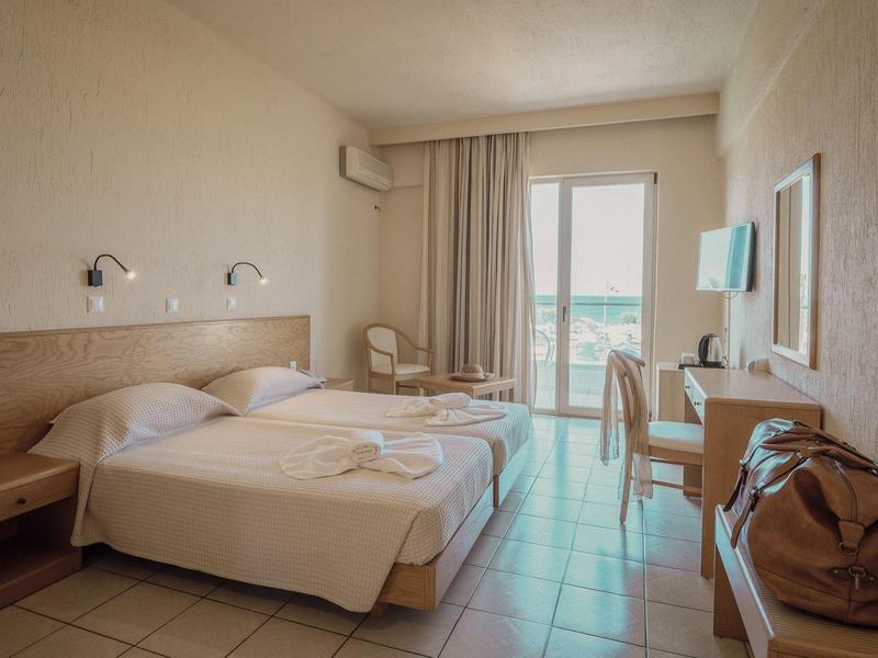 Hotelzimmer mit zwei Einzelbetten, Schreibtisch, Balkon und neutralen Wandfarben.