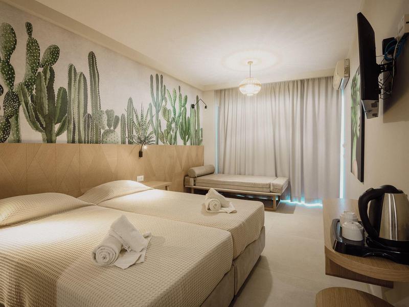 Hotelzimmer mit zwei Einzelbetten, Kaktus-Wanddeko, Vorhängen und Teekocher auf Holzablage.