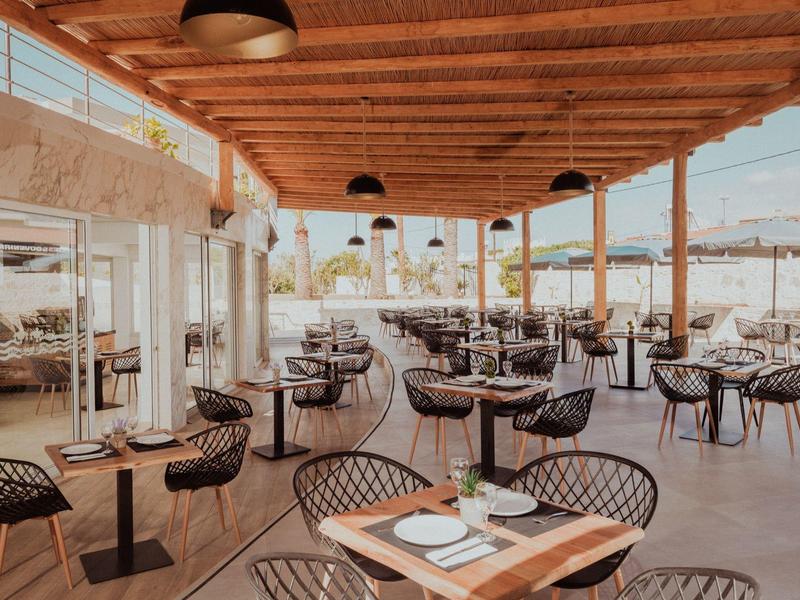 Offenes Restaurant mit Holzdecke, schwarzen Stühlen und Holztischen, sonnige Atmosphäre.