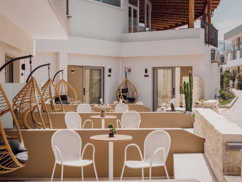 Moderner Außenbereich mit weißen Stühlen, runden Tischen und hängenden Korbsesseln aus Rattan.