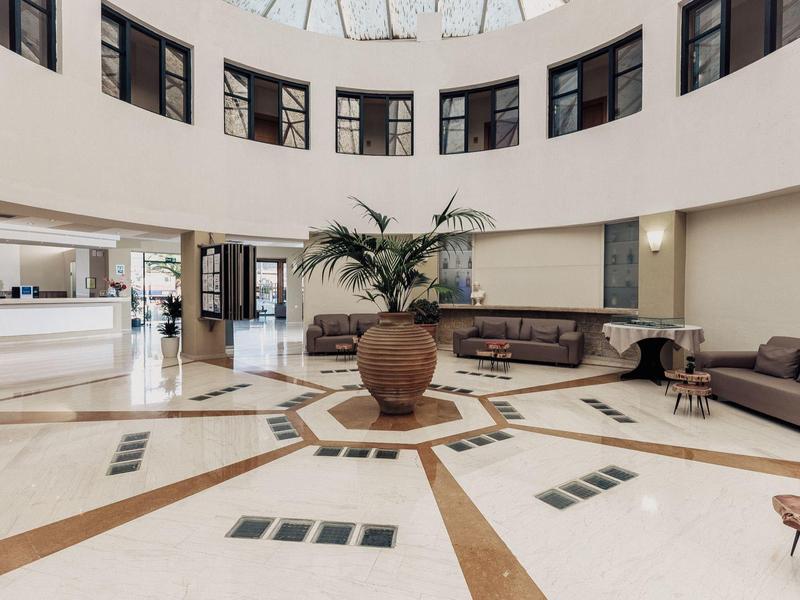 Runder heller Empfangsbereich mit Ledersofas, großem Topf mit Palme und gläserner Kuppel.