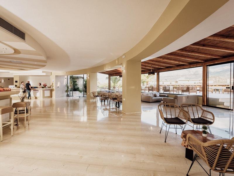 Helle, moderne Lounge mit Holz- und Korbmöbeln, großen Fenstern und Blick auf das Meer.