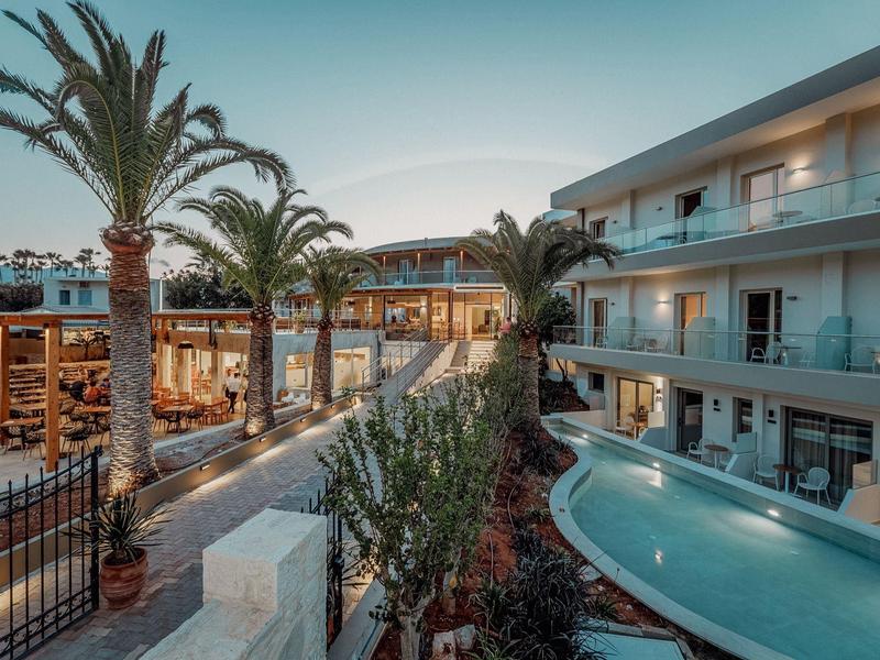 Moderner Hotelkomplex mit Swimmingpool, Palmen und Außenrestaurant bei Abenddämmerung.