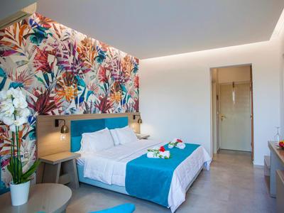 Nowoczesny pokój hotelowy z niebieską narzutą, kolorowym wzorem kwiatowym na ścianie, stolikiem nocnym i orchideą.