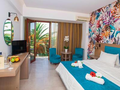 Nowoczesny pokój hotelowy z kolorowym wzorem na ścianie, łóżkiem podwójnym i balkonem z widokiem na rośliny.