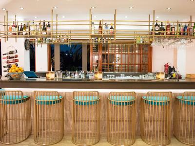 Nowoczesny bar hotelowy z bambusowymi stołkami i wiszącymi półkami z butelkami.