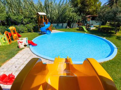 Piscina rotonda con area giochi e scivolo giallo in un giardino verde.