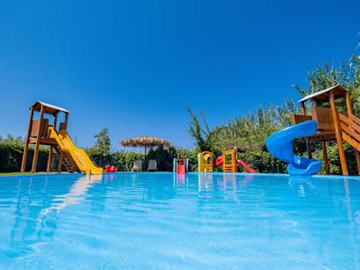 Plenerowy basen dla dzieci z dwoma zjeżdżalniami pod bezchmurnym niebem.