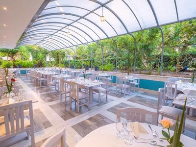 Terrazza esterna coperta di un hotel con tavoli e sedie bianchi in una zona giardino.
