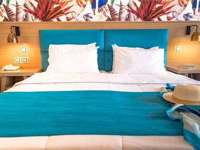 Camera d'hotel moderna con letto matrimoniale, copriletto turchese e decorazioni murali colorate.