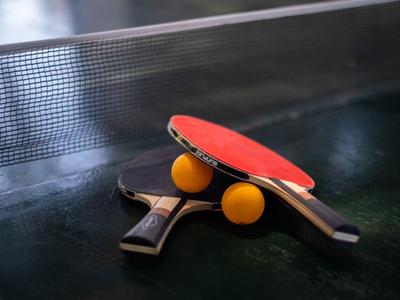 Zwei Tischtennisschläger und zwei orangene Bälle auf einem grünen Tischtennistisch.
