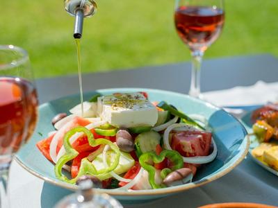 Bunter Salatteller mit frischem Gemüse und Feta, begleitet von Gläsern Rotwein auf gedecktem Tisch im Freien.