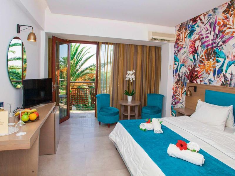 Nowoczesny pokój hotelowy z kolorowym wzorem na ścianie, łóżkiem podwójnym i balkonem z widokiem na rośliny.