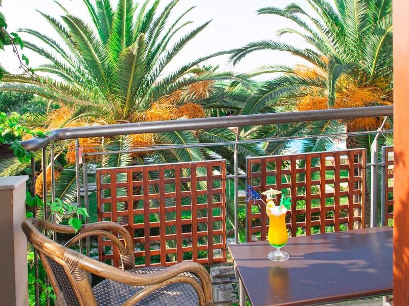 Balkon z wiklinowym krzesłem, stołem i tropikalnymi palmami w tle w słoneczny dzień.