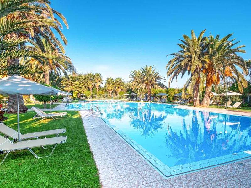 Duży basen z leżakami i parasolami otoczony palmami pod czystym niebem.