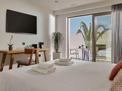 Moderne hotelkamer met bed, tv, bureau en balkon met uitzicht op palmbomen.