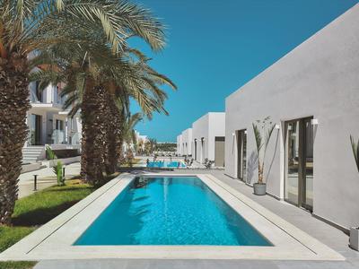 Moderne buitenzwembad met helder blauw water naast wit hotelgebouw en palmbomen.