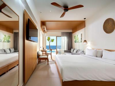 Moderne hotelkamer met tweepersoonsbed, zitgedeelte en zeezicht door grote ramen.