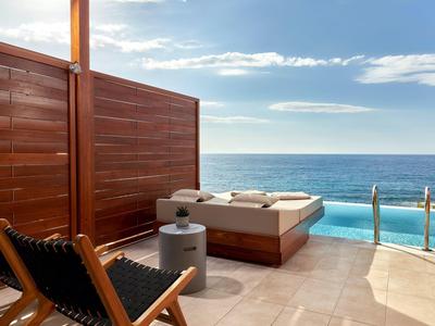 Terrazza con piscina, lettini e vista sull'oceano sotto un cielo azzurro.