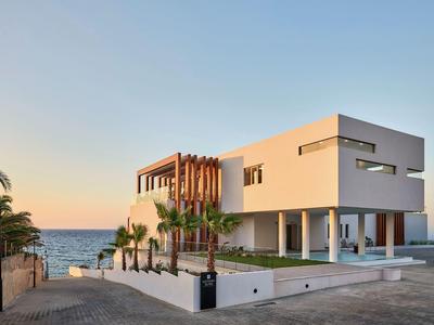 Modern wit vakantiehuis met zeezicht en palmbomen bij zonsondergang.