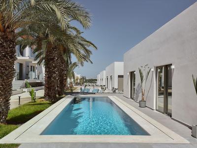 Modern outdoor pool with white buildings and palm trees in a sunny hotel garden.
