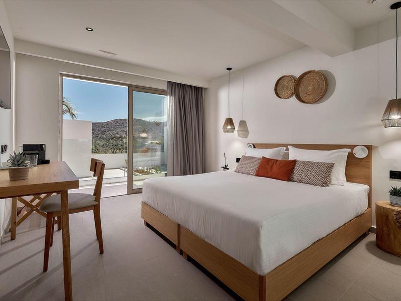 Modern hotelkamer met tweepersoonsbed, bureau en balkon met uitzicht op bergen.