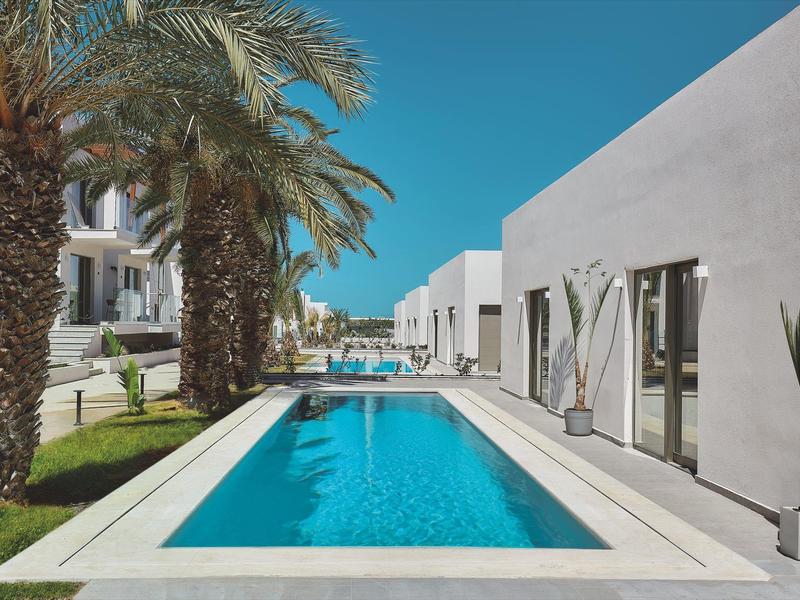 Moderne buitenzwembad met helder blauw water naast wit hotelgebouw en palmbomen.