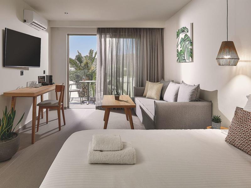 Moderne hotelkamer met bed, bank, bureau, balkon en minimalistische inrichting.