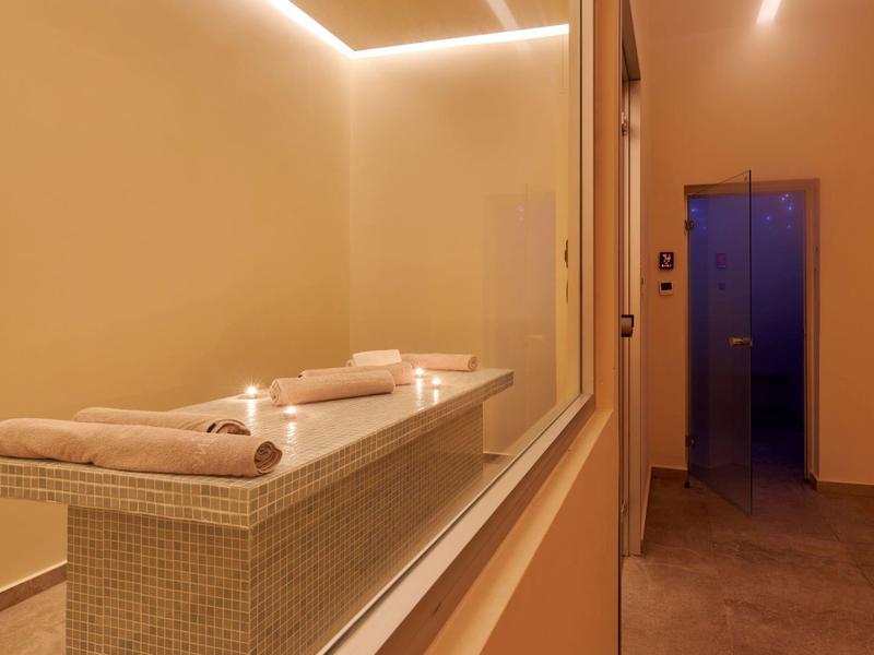 Kamer met een lange beklede ontspanningstafel en zachte verlichting voor spabehandelingen.