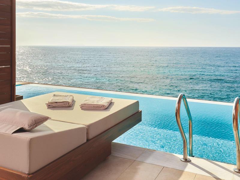 Luxe bed naast een infinity pool met uitzicht op zee bij zonsondergang.