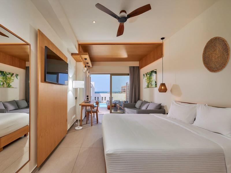 Modern hotelkamer met groot bed, bank en balkon met uitzicht op zee.