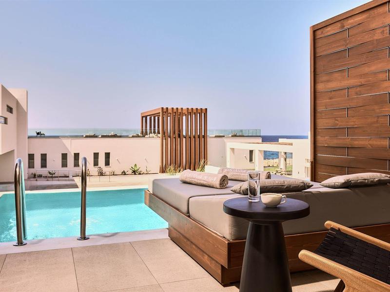 Moderne terras met zwembad, lounge meubels en zeezicht bij zonsondergang.