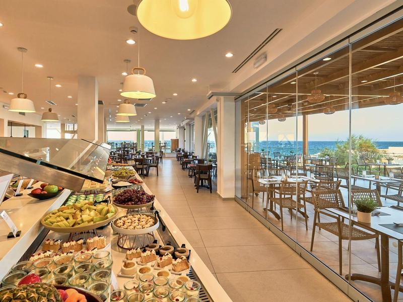 Lichte eetzaal met buffet en terras met uitzicht op zee.