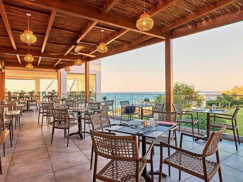 Overdekt terras met tafels en stoelen met uitzicht op zee bij zonsondergang.