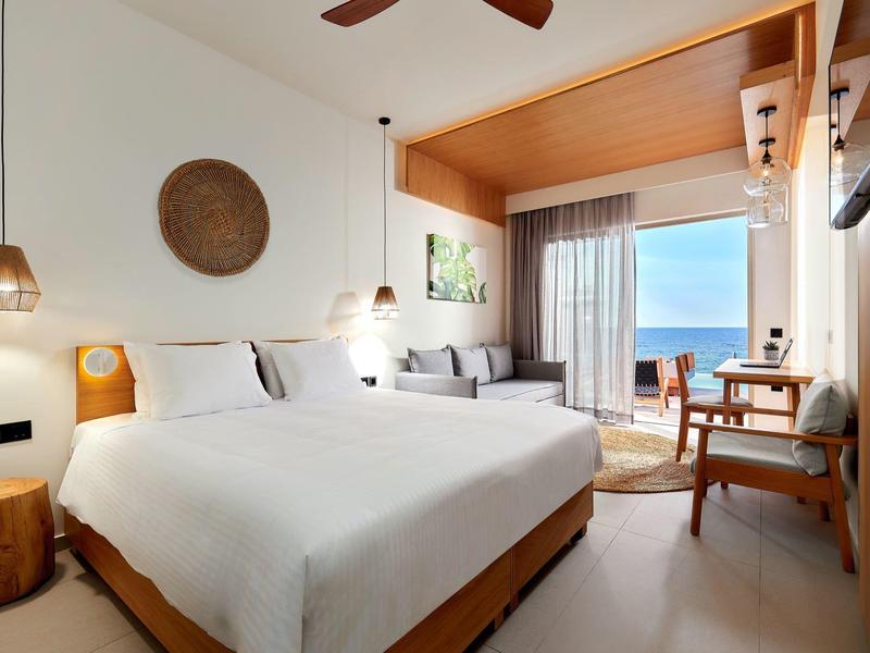 Moderne hotelkamer met groot bed, zithoek en balkon met zeezicht.