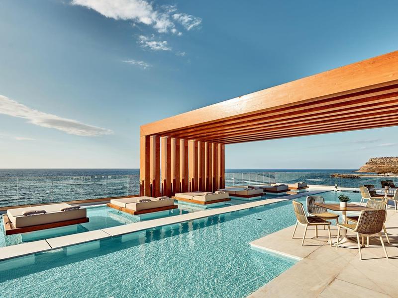 Modern zwembad met houten pergola en zeezicht onder een heldere hemel.