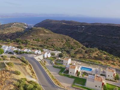Paysage avec collines, routes et bâtiments près d'une zone côtière avec la mer en arrière-plan.