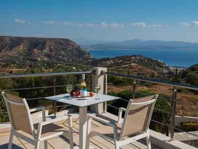Terrazza con tavolo e sedie con vista su colline e mare sotto un cielo limpido.