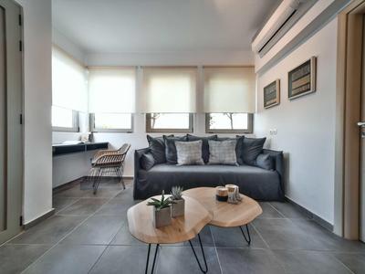 Salon moderne avec canapé gris, deux tables en bois et bureau près de la fenêtre.