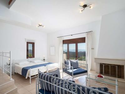 Chambre d'hôtel lumineuse avec lit double, canapé, cheminée et vue sur la mer.