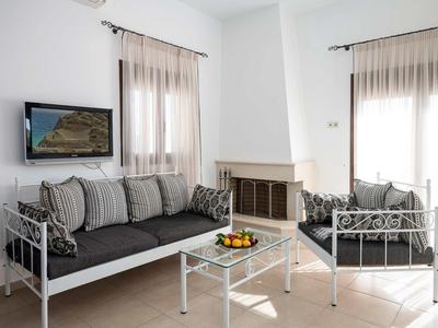 Salon avec deux canapés gris, table en verre, cheminée et télévision sur murs blancs.