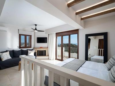 Camera moderna con letto matrimoniale, divano e vista sul mare attraverso grandi finestre.