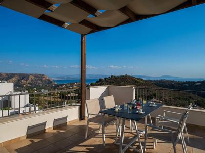 Terrazza con sedie e tavolo sotto tenda da sole con vista sul mare e cielo sereno.