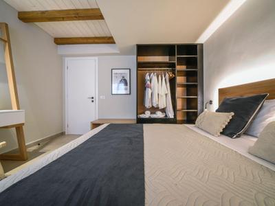 Dormitorio moderno con vigas de madera, armario abierto y cama acogedora con almohadas.